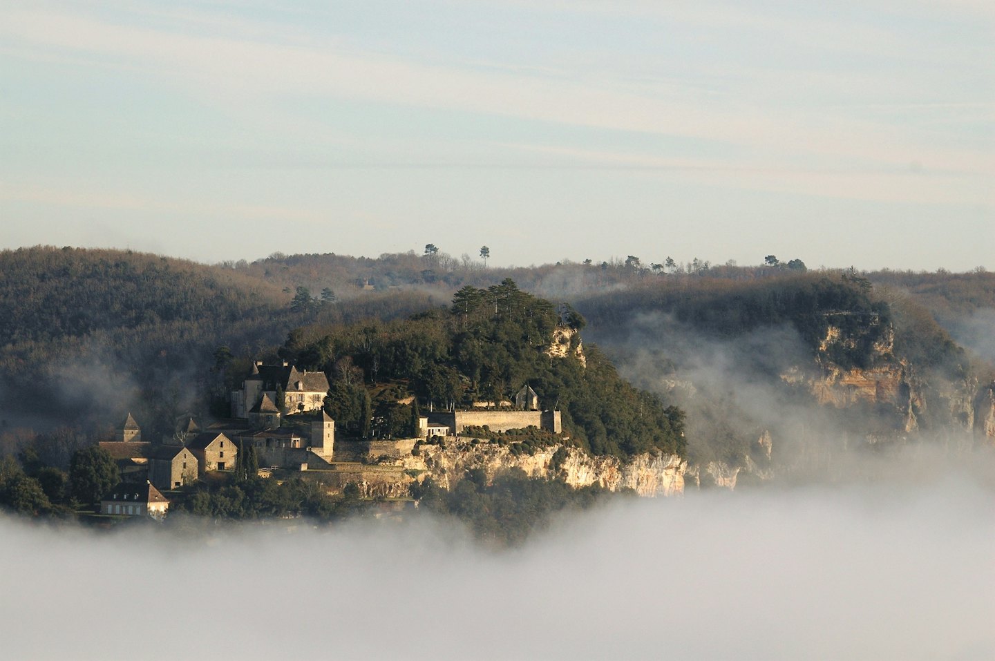 Villaggio di pietra su una scogliera sopra una valle coperta di nebbia.