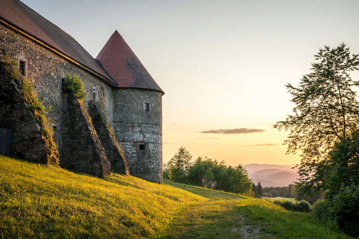 Castello storico in pietra con tetto di tegole rosse su una collina erbosa.