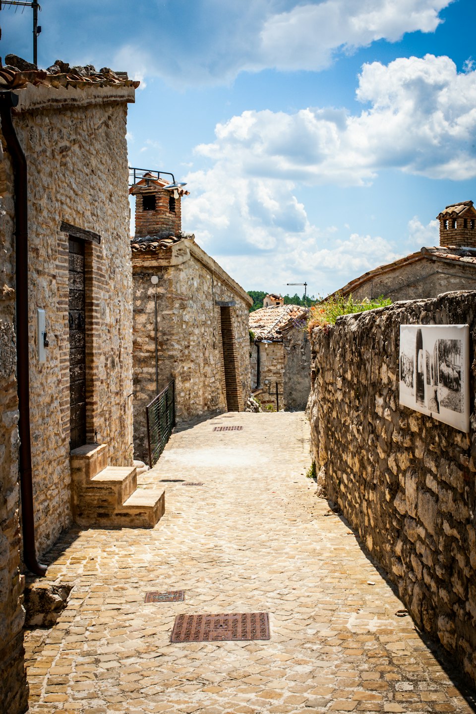 Sentiero acciottolato illuminato dal sole che serpeggia tra storici edifici in pietra.