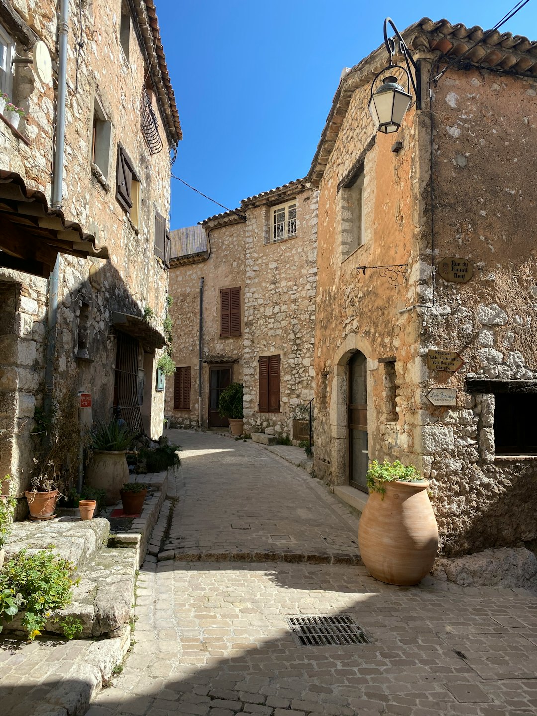 Vicolo acciottolato illuminato dal sole in un borgo storico con vasi in terracotta.