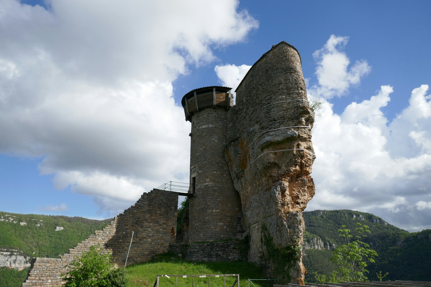 Rovine di un castello medievale in pietra si ergono su una collina verde che domina una valle.